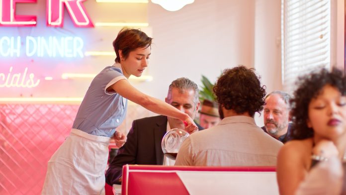 Waitress Pouring Coffee For Customers In 1950s Styled Diner