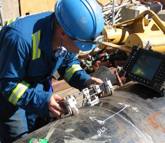 At a construction site, a technician tests a pipeline weld for defects using an ultrasonic phased array instrument.