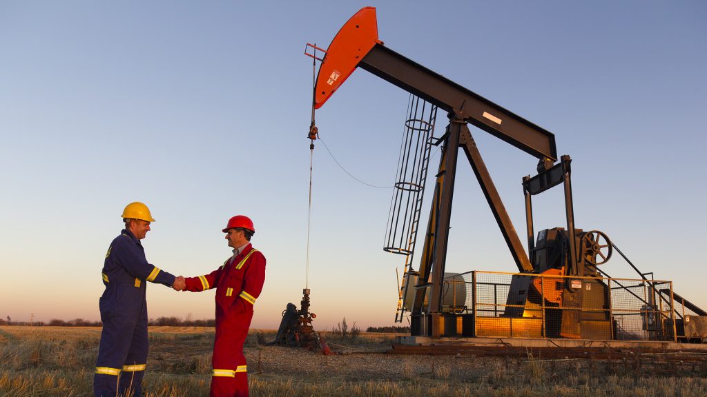 Oil field workers in front of oil derrick