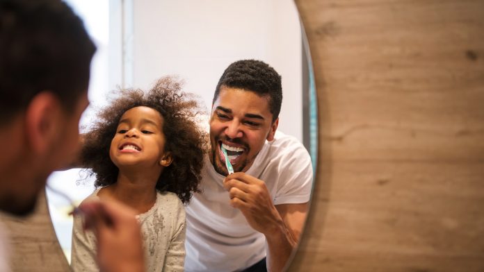 Dad showing daughter how to brush teeth