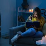Woman Reading During Power Outage With Flashlight and Candles