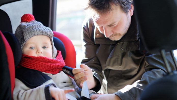 Father helps his son to fasten belt on car seat