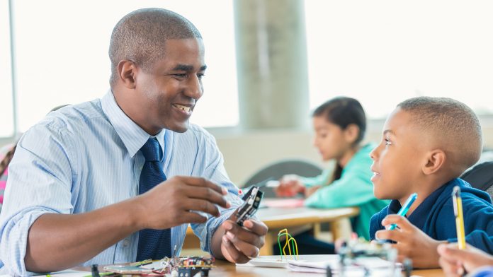 Man is teaching elementary little boy about robotics during school STEM program