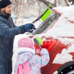 Father and daughter removing snow from car windows