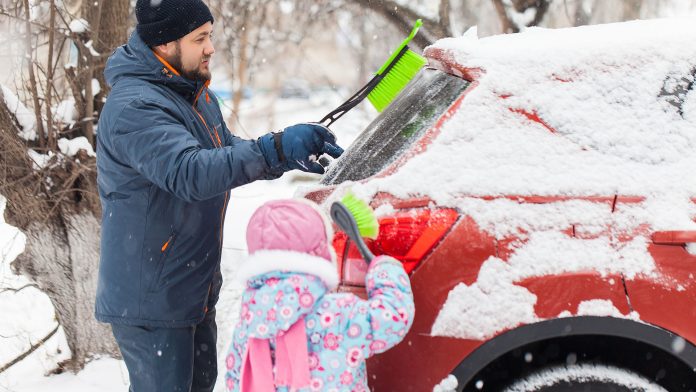 Father and daughter removing snow from car windows