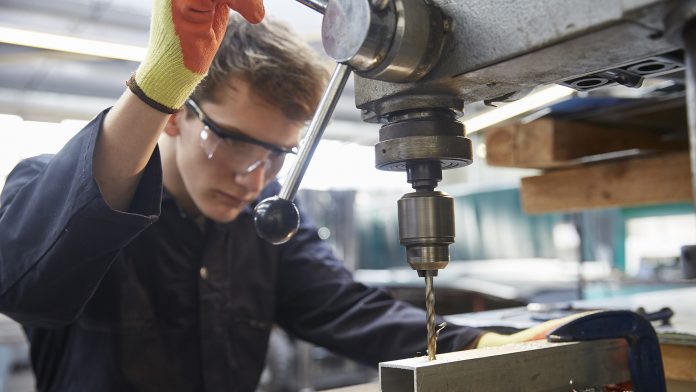 Young apprentice using pillar drill in steel fabrication factory