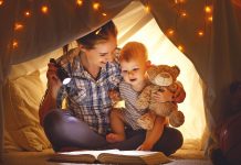 Mother and baby son with a book and a flashlight before going to bed