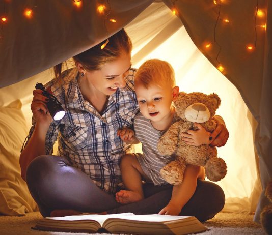 Mother and baby son with a book and a flashlight before going to bed