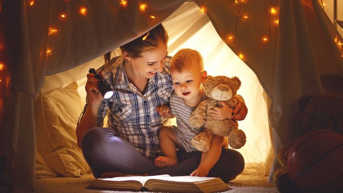 Mother and baby son with a book and a flashlight before going to bed
