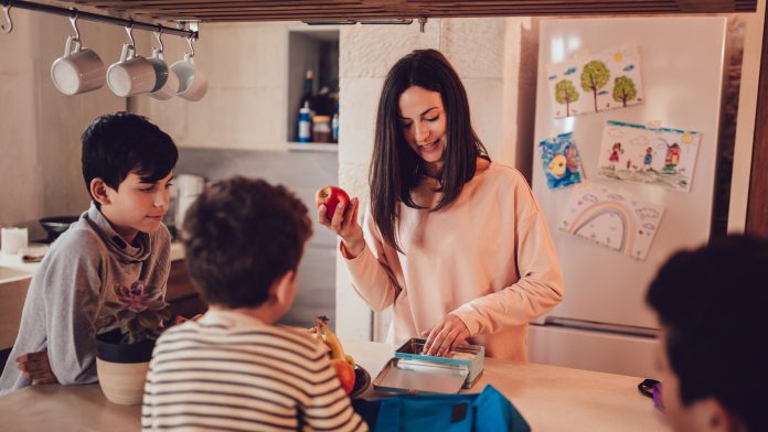 Mother preparing healthy food lunch boxes for children in kitchen