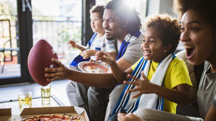 Cheerful black family cheering while watching rugby match on TV at home. football