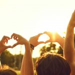 Hands of group friends in the shape of a heart against the sunset