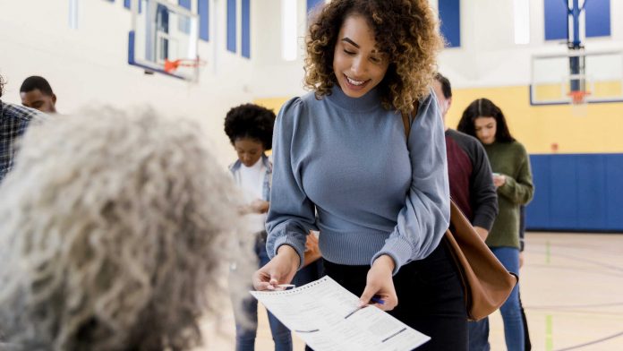 Unrecognizable mature woman assists mid adult woman with voting document super tuesday