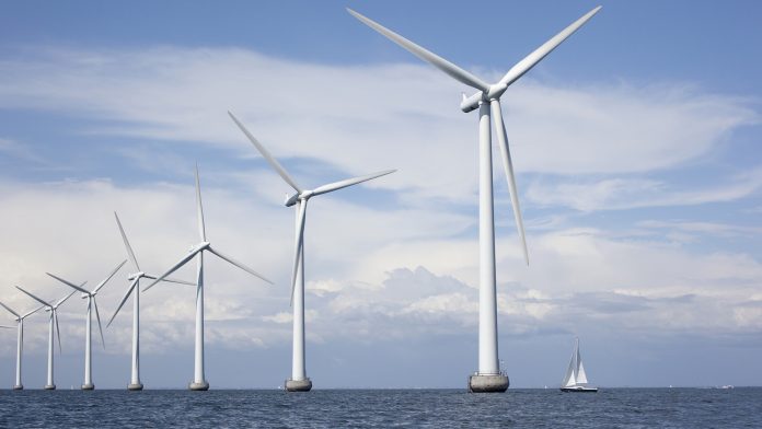 Large white windmills in the sea with a sailboat