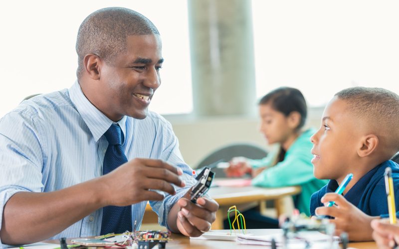 Man is teaching elementary little boy about robotics during school STEM program