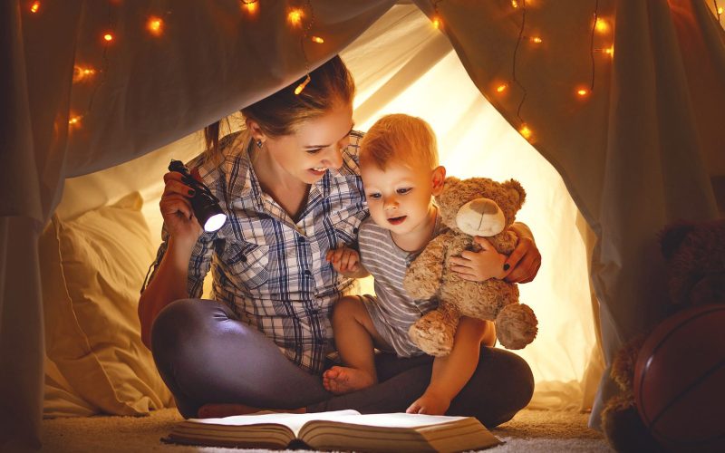 Mother and baby son with a book and a flashlight before going to bed