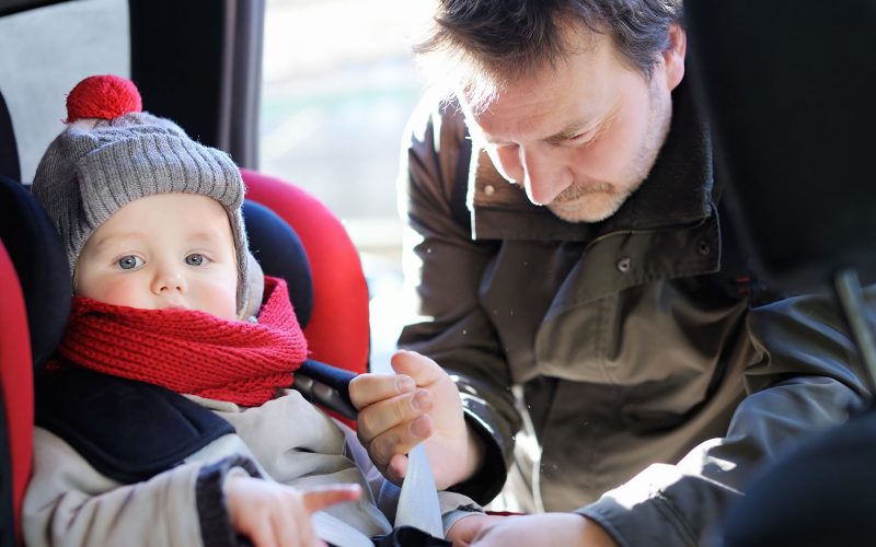 Father helps his son to fasten belt on car seat