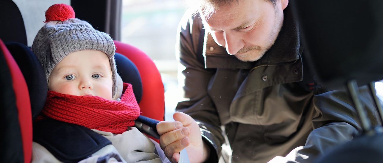 Father helps his son to fasten belt on car seat