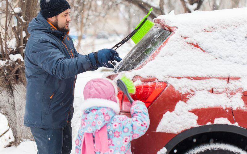 Father and daughter removing snow from car windows