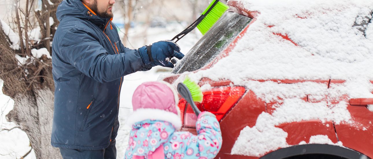 Father and daughter removing snow from car windows