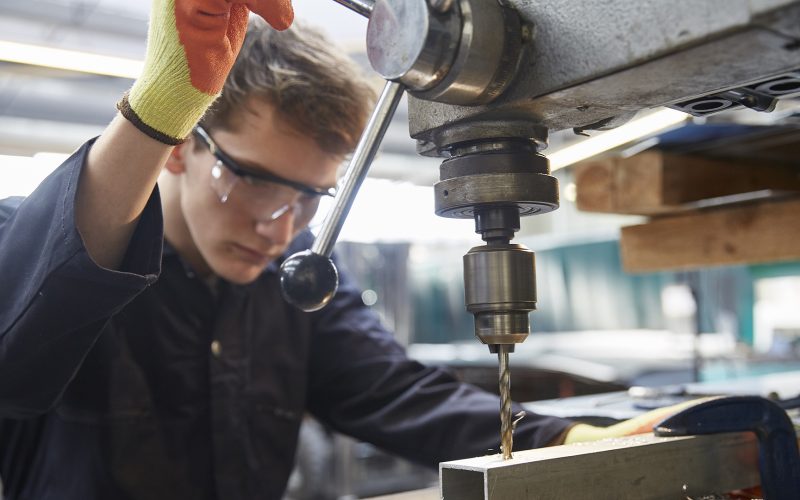 Young apprentice using pillar drill in steel fabrication factory