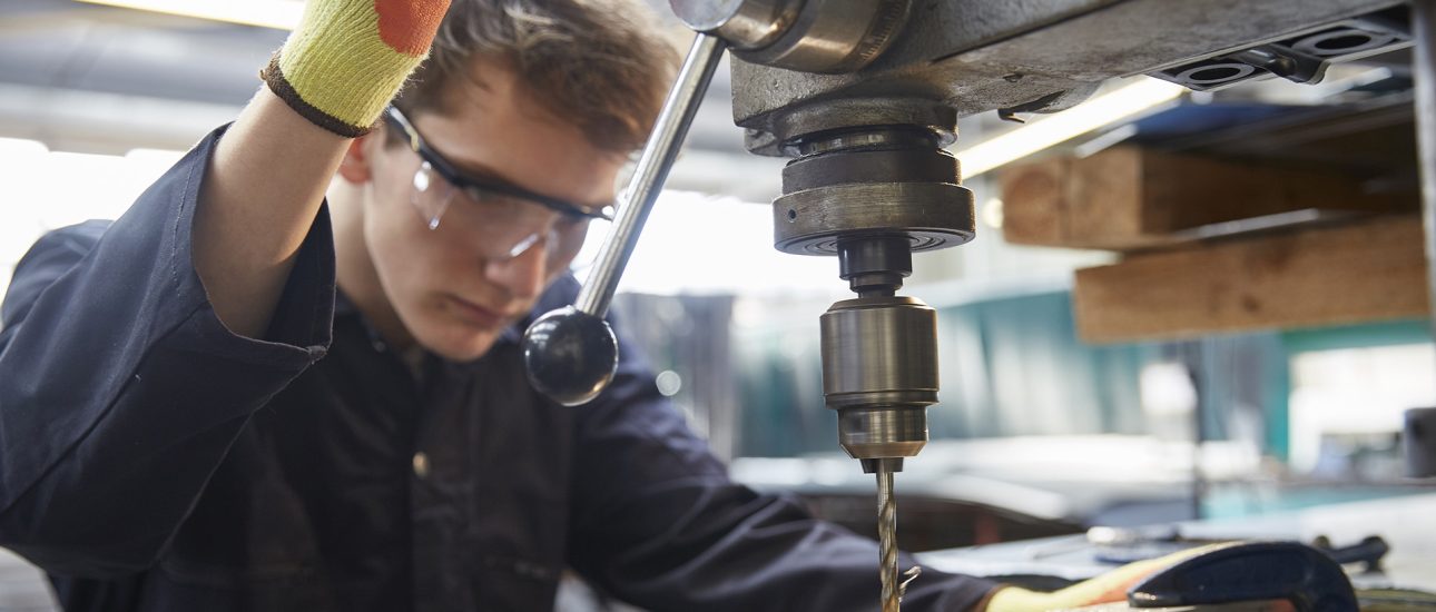 Young apprentice using pillar drill in steel fabrication factory