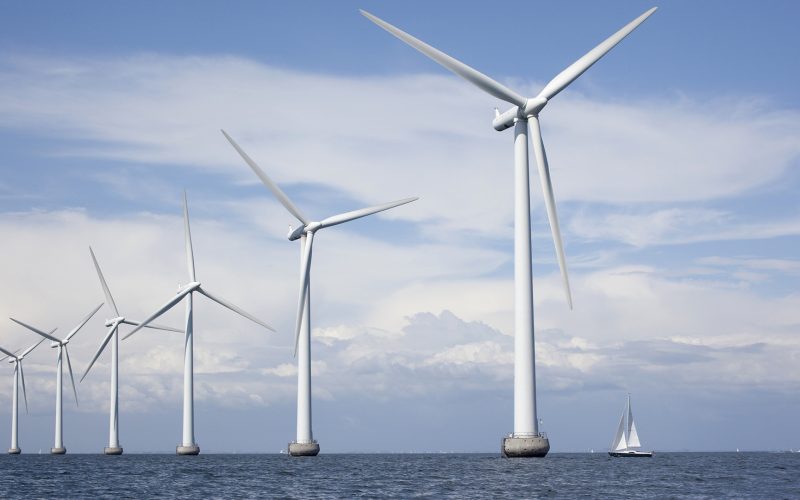 Large white windmills in the sea with a sailboat