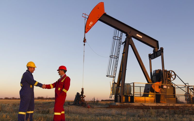 Oil field workers in front of oil derrick