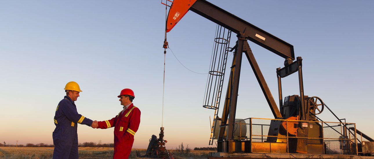 Oil field workers in front of oil derrick