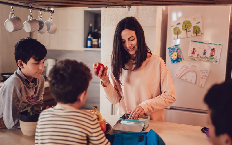 Mother preparing healthy food lunch boxes for children in kitchen