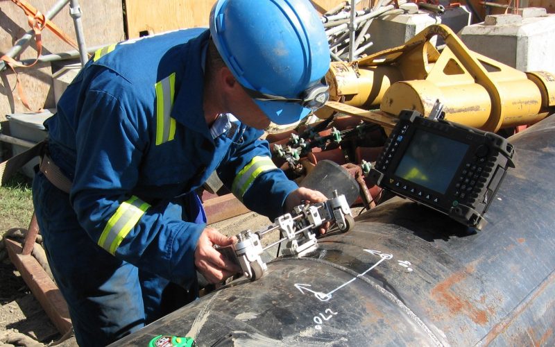 At a construction site, a technician tests a pipeline weld for defects using an ultrasonic phased array instrument.